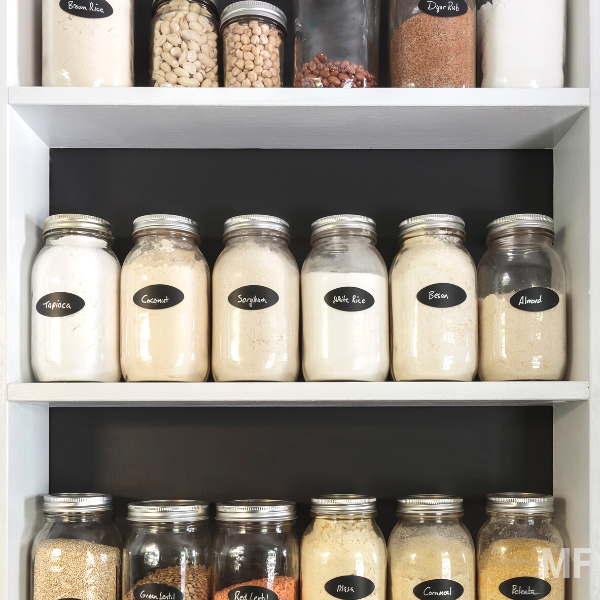 Jars of flours and grains on white shelves in pantry.